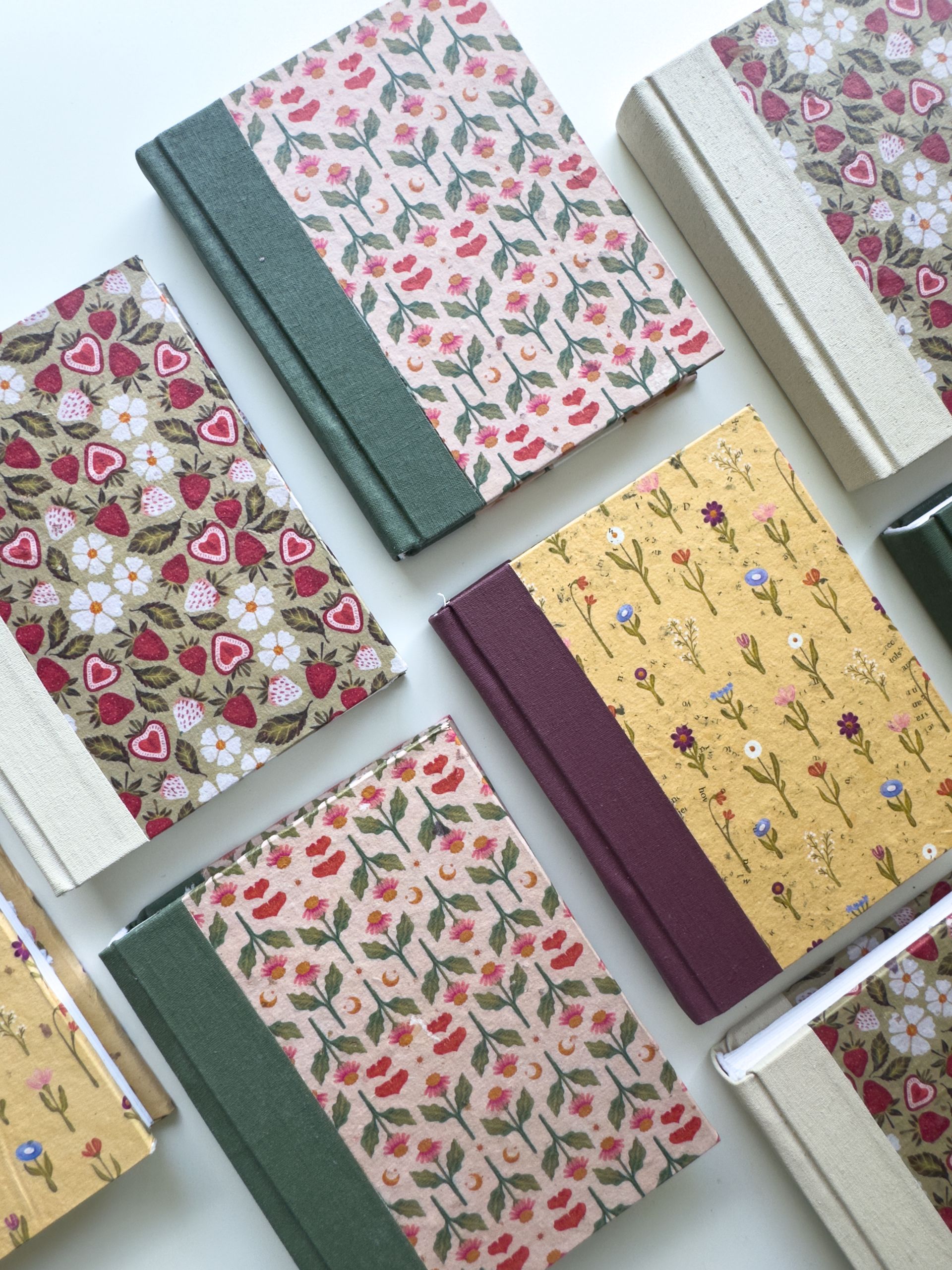 Six small, fabric-covered journals with floral and strawberry patterns arranged in a top-down view.