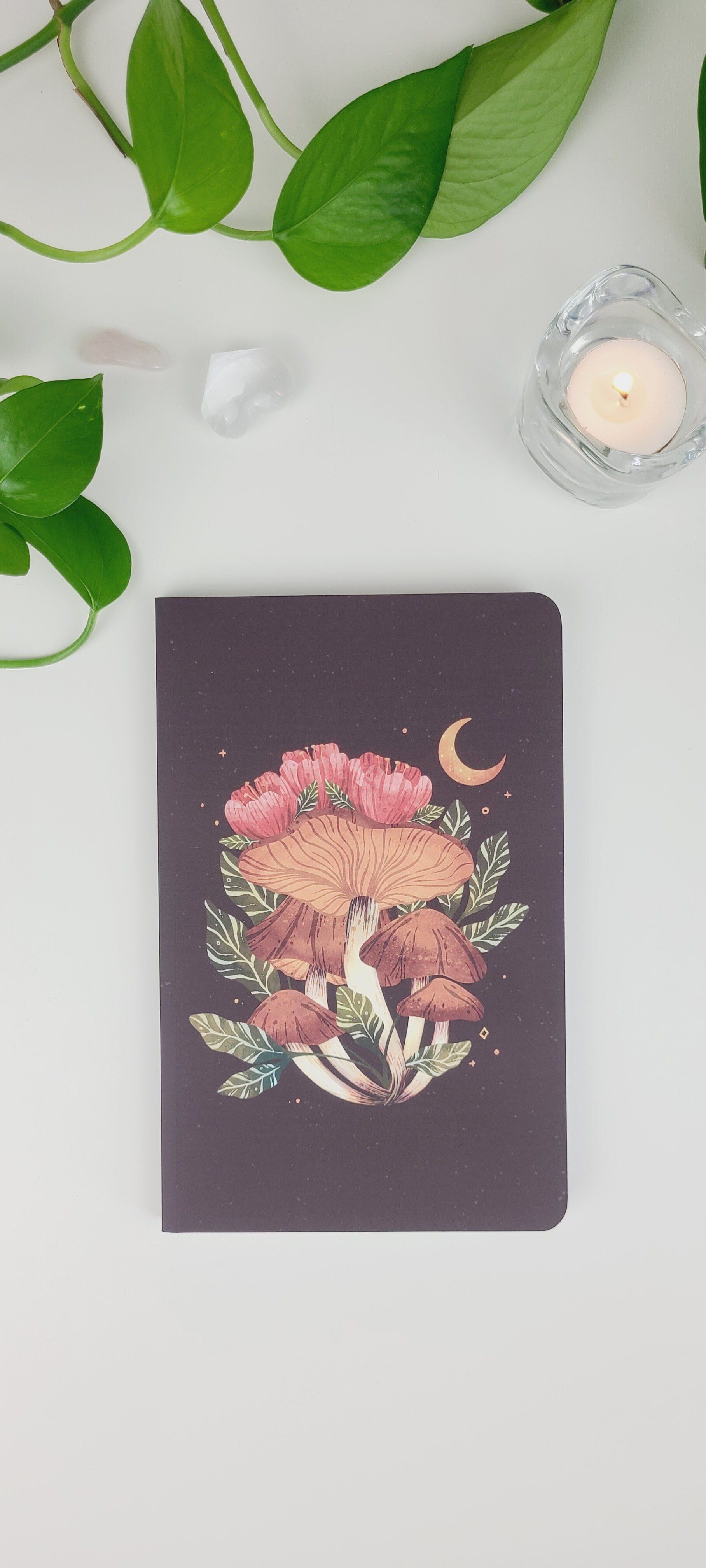 a notebook with a picture of mushrooms and flowers on it is sitting on a table .
