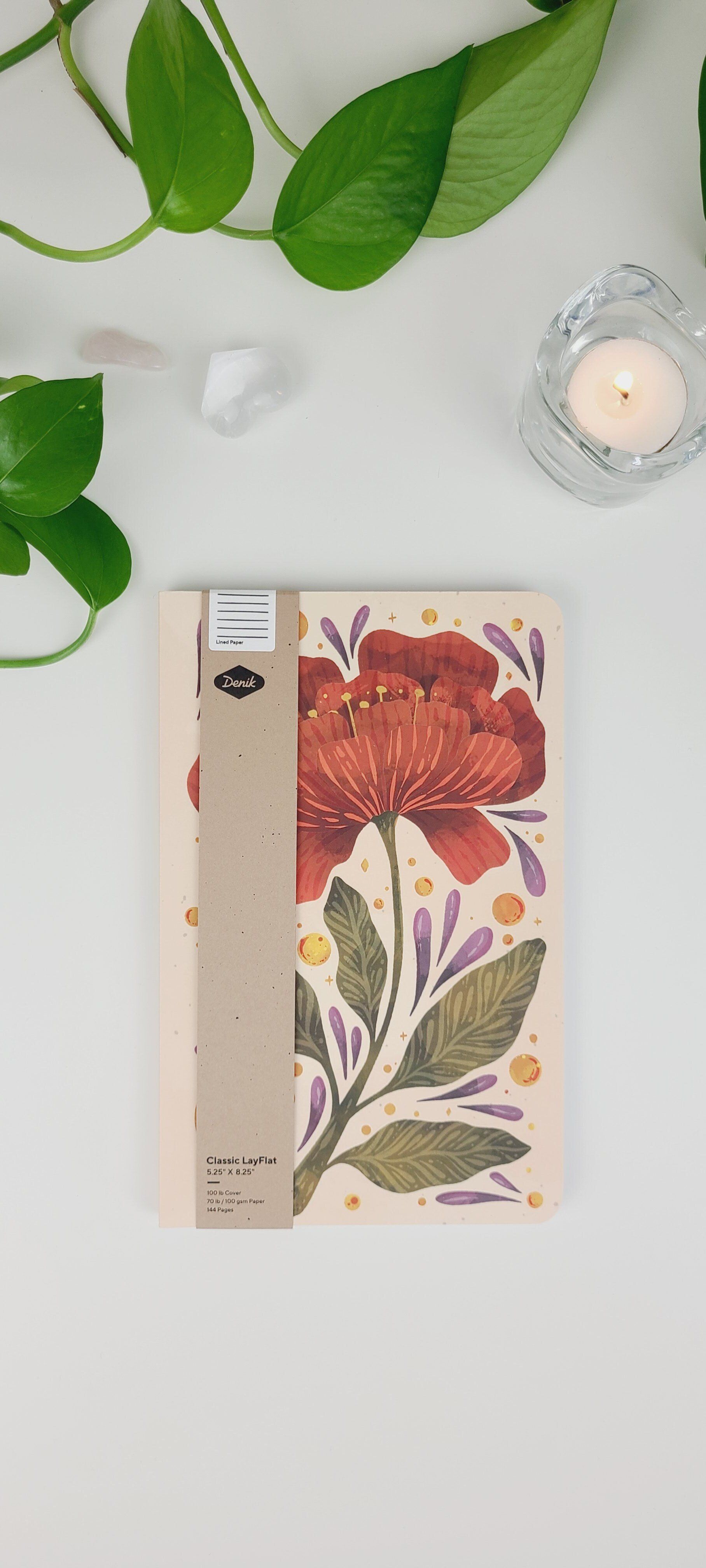 a notebook with a flower on the cover is sitting on a table next to a plant and a candle .