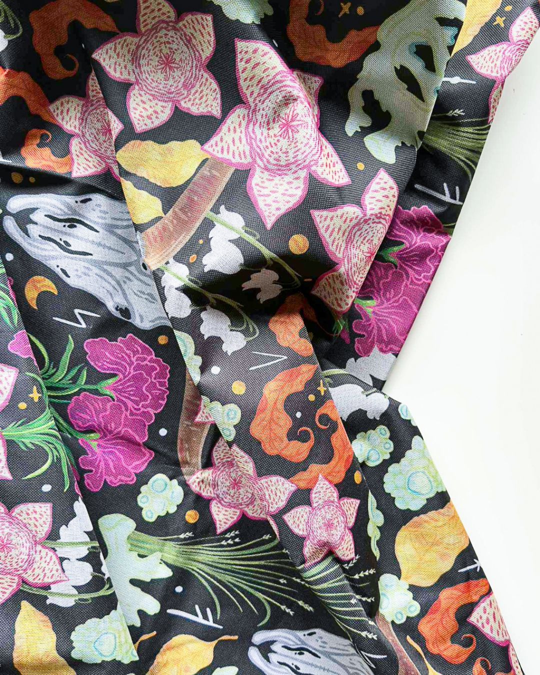 Fabric featuring a dark, patterned print with pink star-shaped flowers, orange abstract shapes, and grey skulls.
