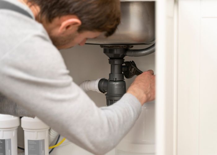 A man is fixing a sink pipe in a kitchen.