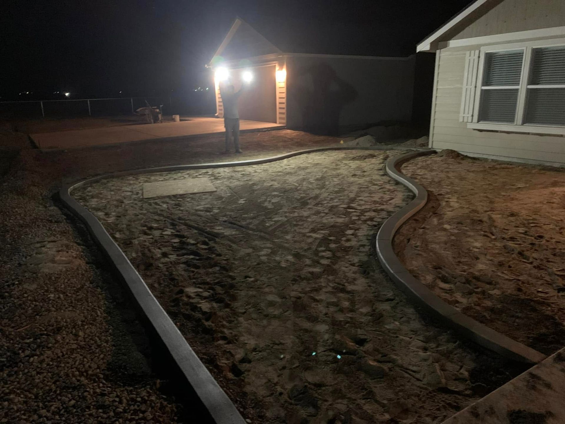 A nighttime view of a newly installed concrete garden border outlining a landscaped area in front of a house.