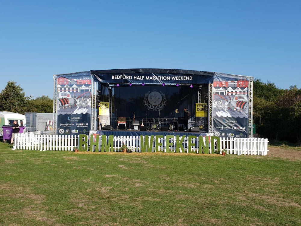 A stage set up with branded banners on the back, top and PA wings for the Bedford Running Festival
