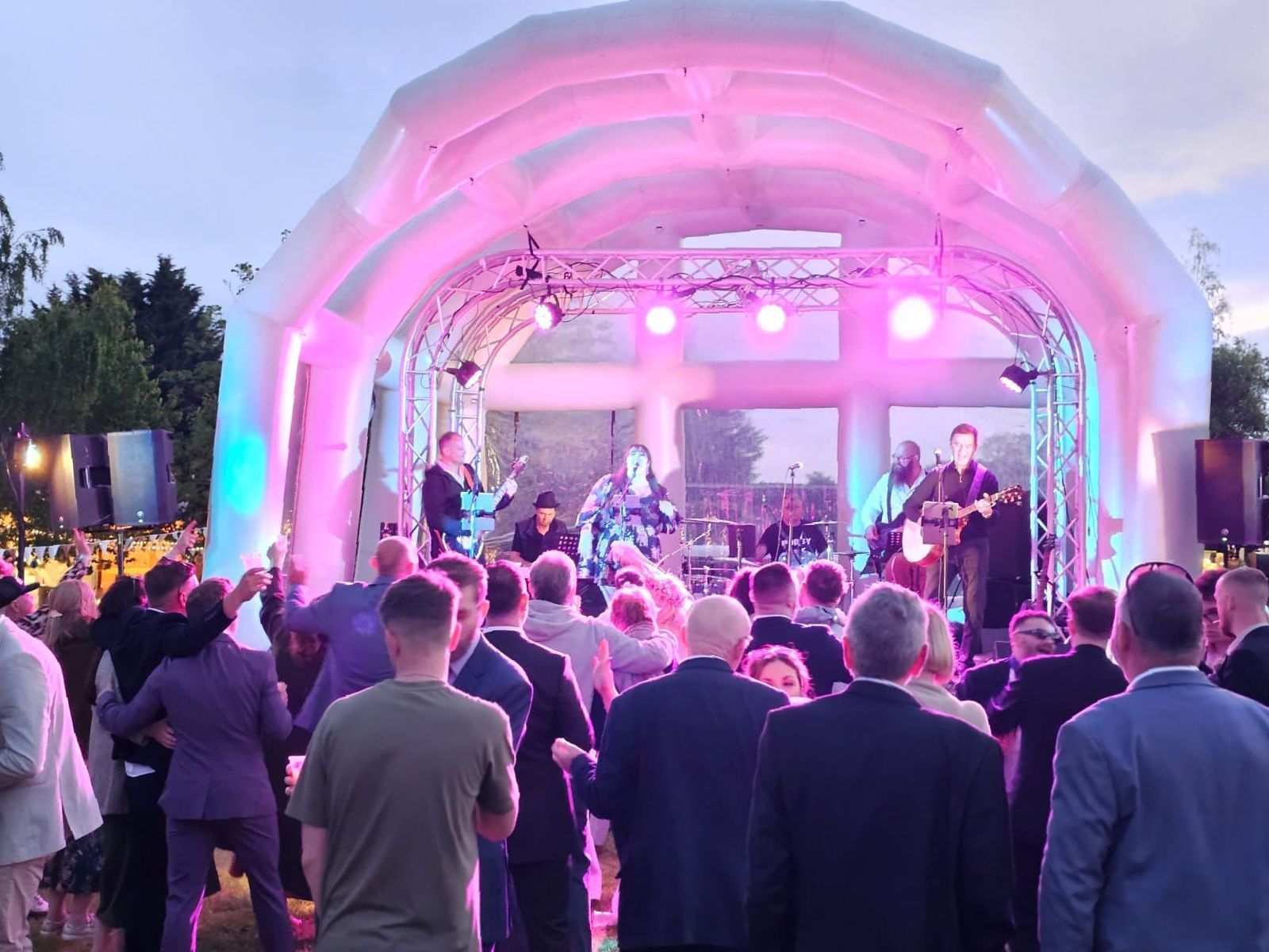 an inflatable stage at a festial wedding, with pink lights on stage, a band playing and guests watching