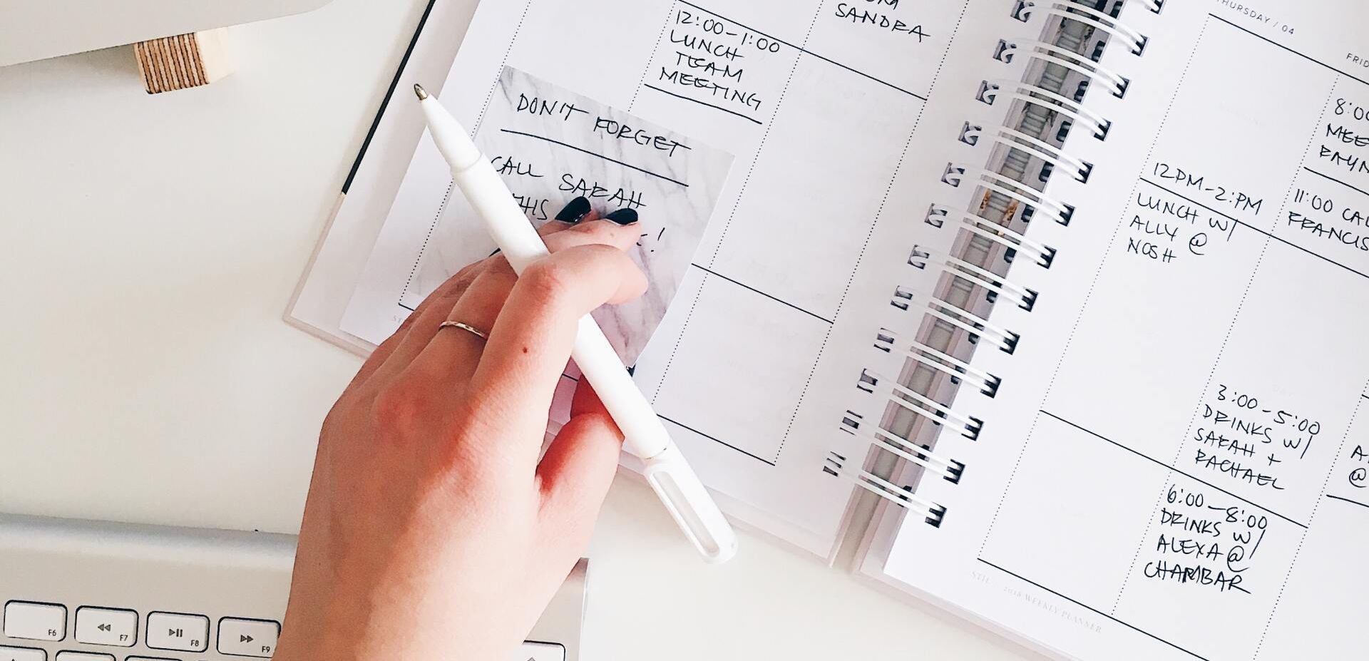 A close up of someone writing in a diary with a pen, everything is white apart from the hand.
