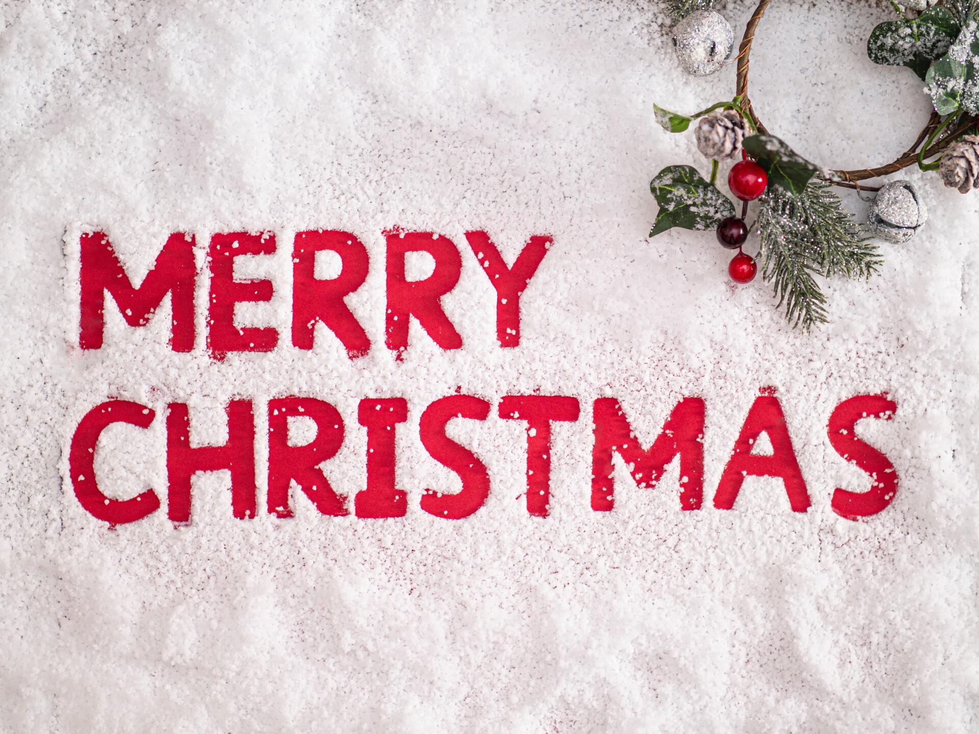 Merry Christmas written in snow with a wreath in the corner