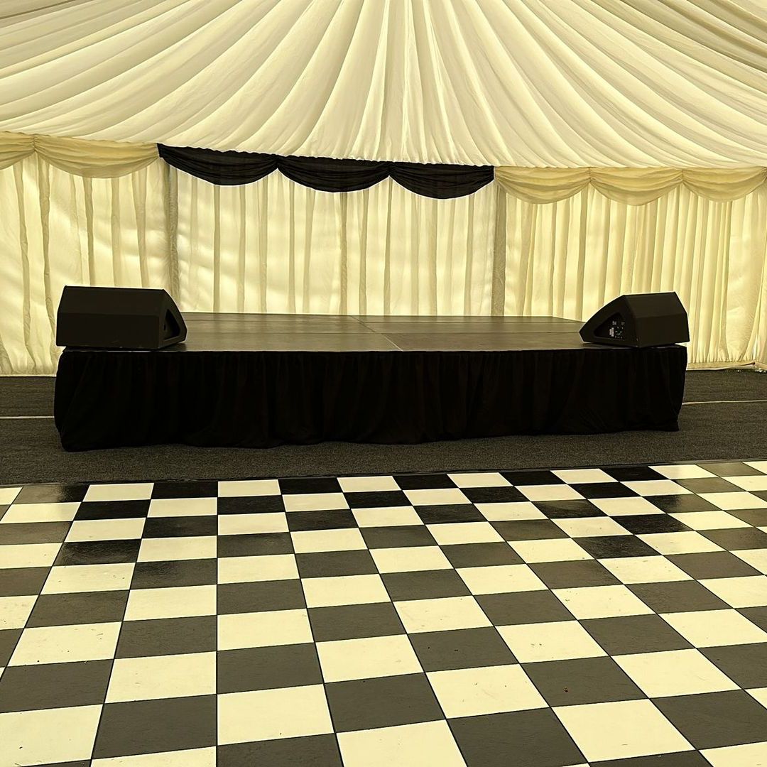 A modular stage inside a white draped marquee with a chequered dance floor