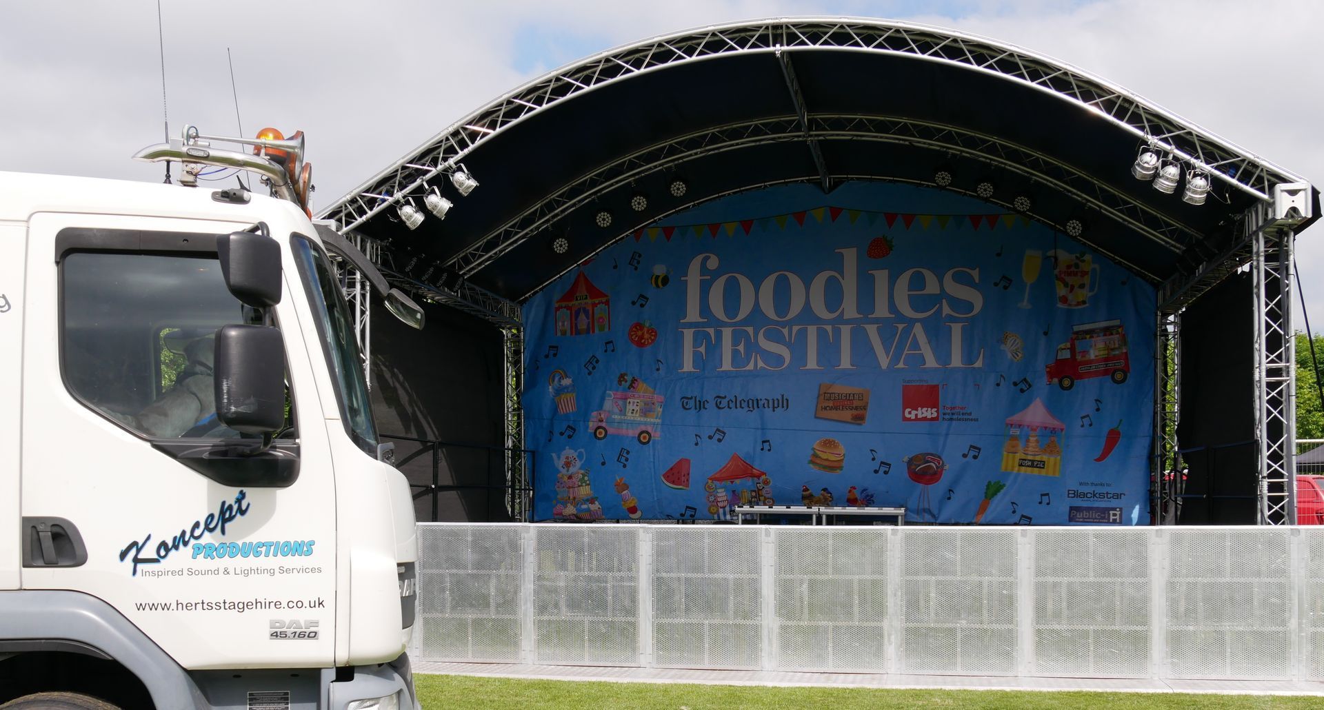 Arc truss stage set up in a field with the Koncept lorry in front of it