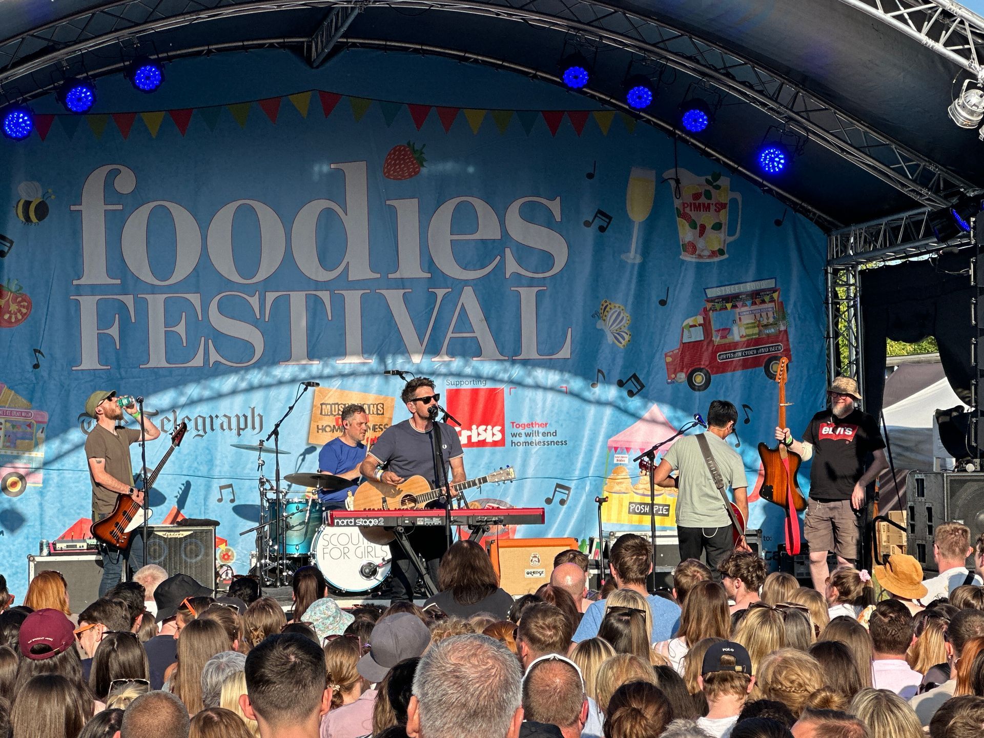 Arc truss stage set up in a field with a banner that says foodies festival and scouting for girls playing on it.