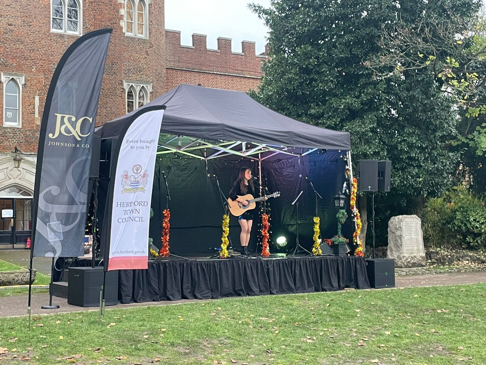 Modular stage set up outside a castle with a black canopy and a performing with a guitar on it.