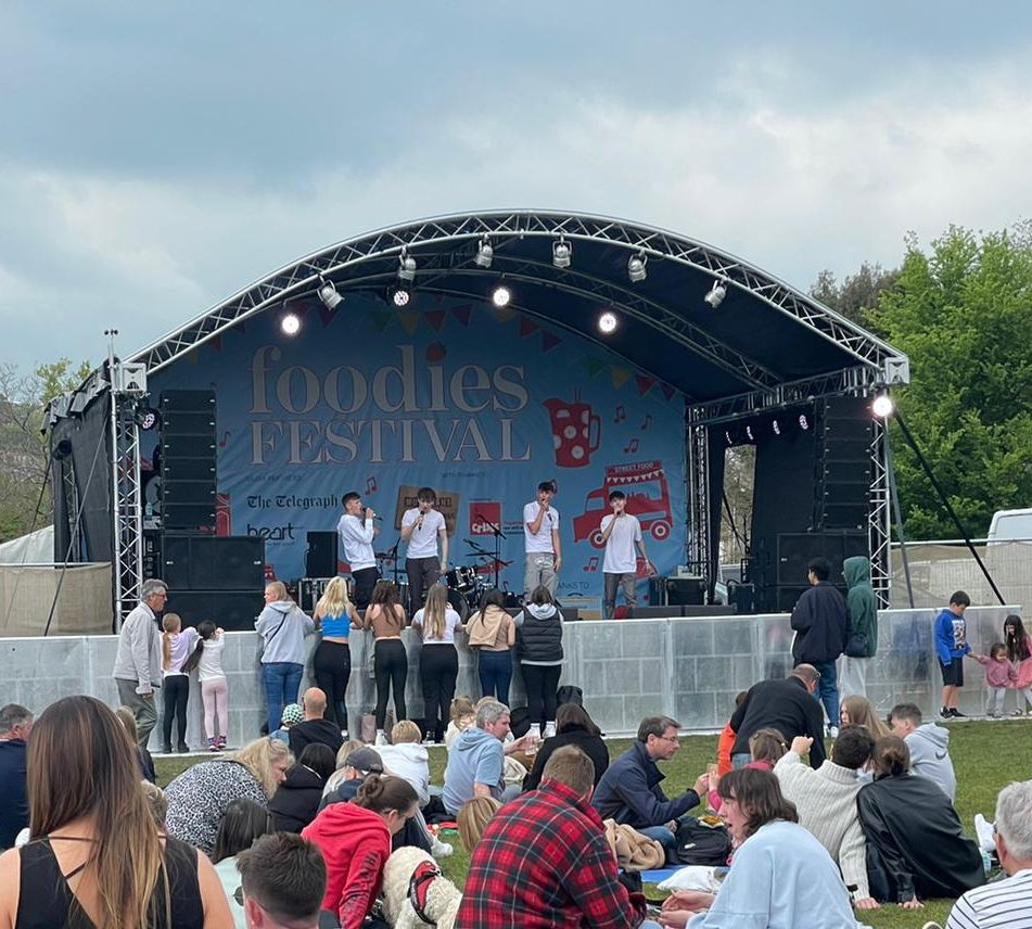 A crowd watching a boy band perform on the arc truss stage at the foodies festival