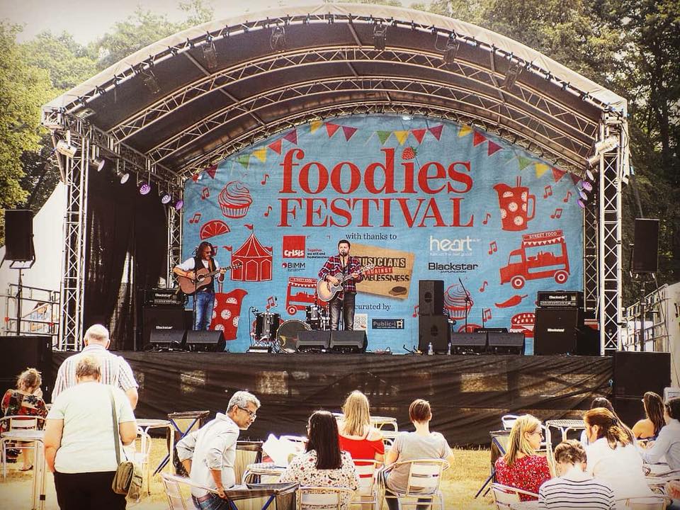 Imagine of an arc truss stage with a back drop reading foodies festival and a and performing on stage.