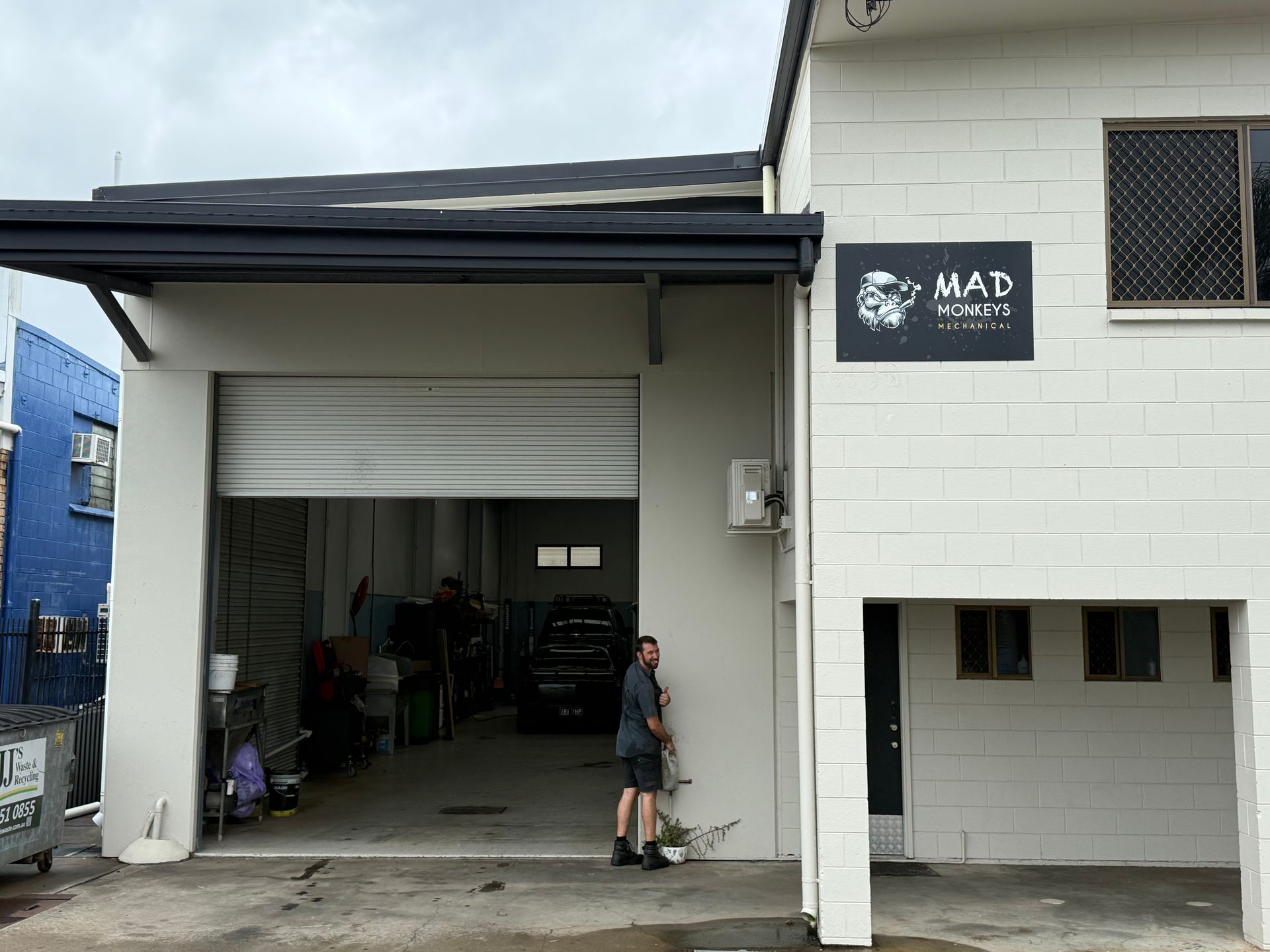 Person Stands by the Open Bay Door of a White Commercial Building — Mad Monkeys Mechanical in Cairns City, QLD
