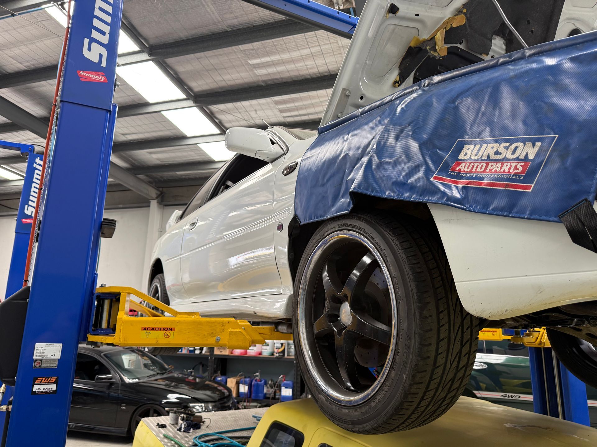 A White Car is Lifted on a Mechanical Hoist Inside a Workshop — Mad Monkeys Mechanical in Cairns City, QLD