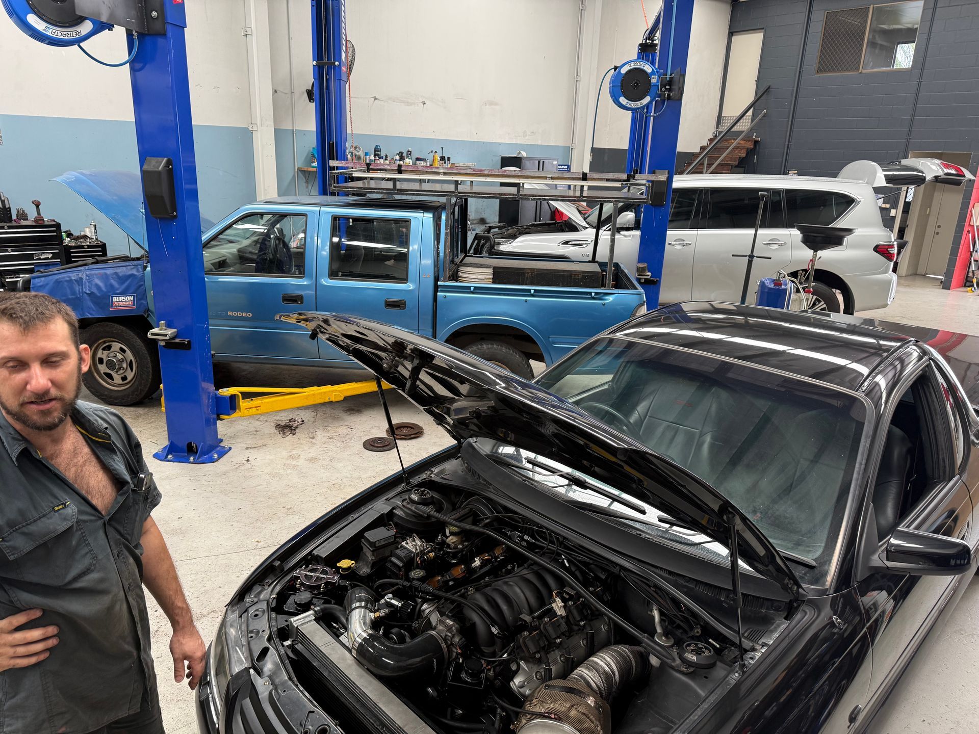 A Mechanic Stands Beside a Car With Its Hood Open in a Garage — Mad Monkeys Mechanical in Cairns City, QLD