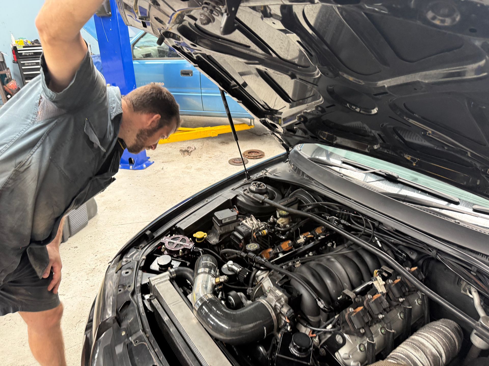 Mechanic in a Grey Uniform Inspects the Open Hood of a Car Inside a Repair Shop — Mad Monkeys Mechanical in Cairns City, QLD
