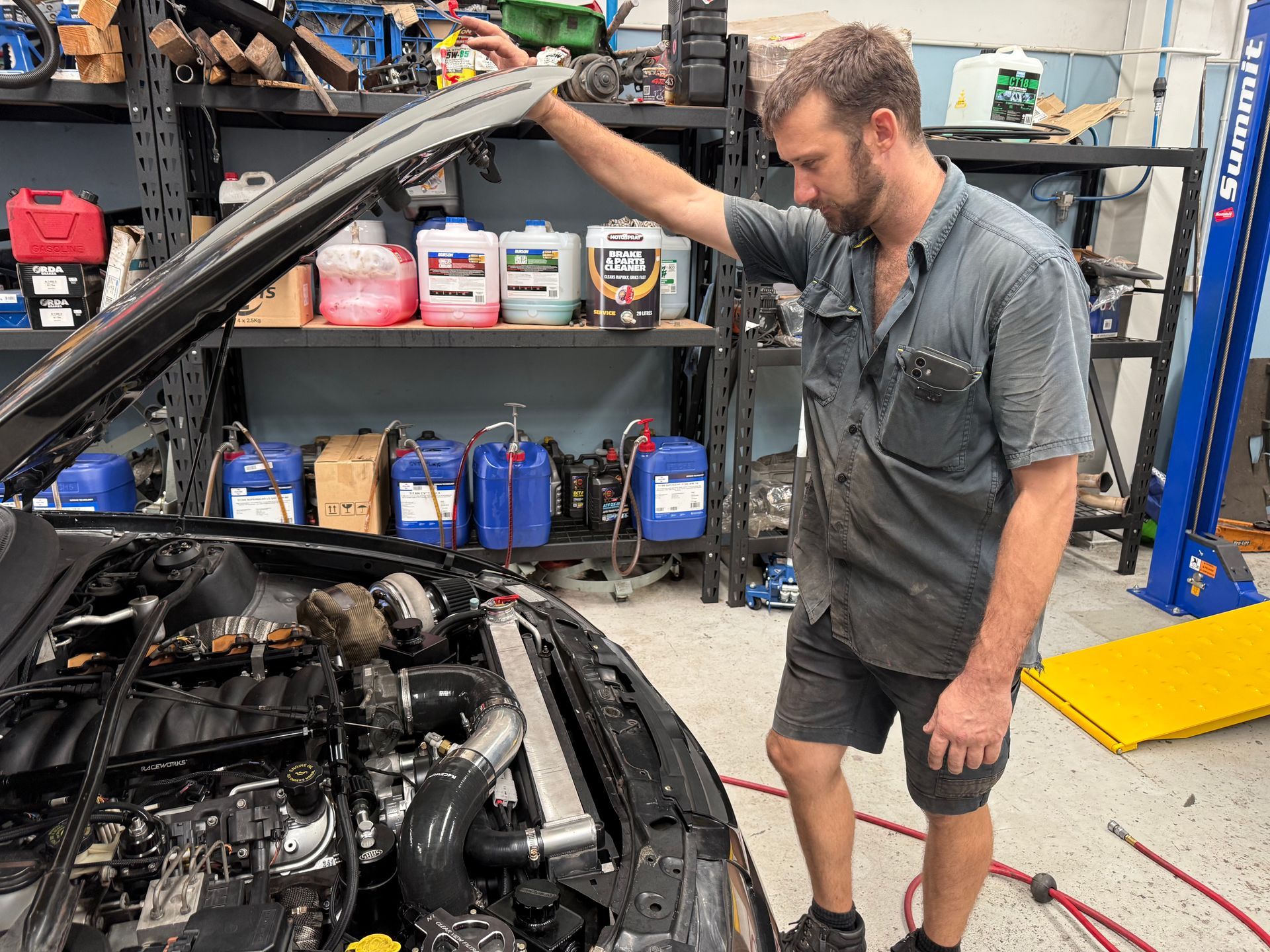 A Person in a Gray Shirt in a Garage Workshop, Holding Up the Open Hood of a Car — Mad Monkeys Mechanical in Cairns City, QLD