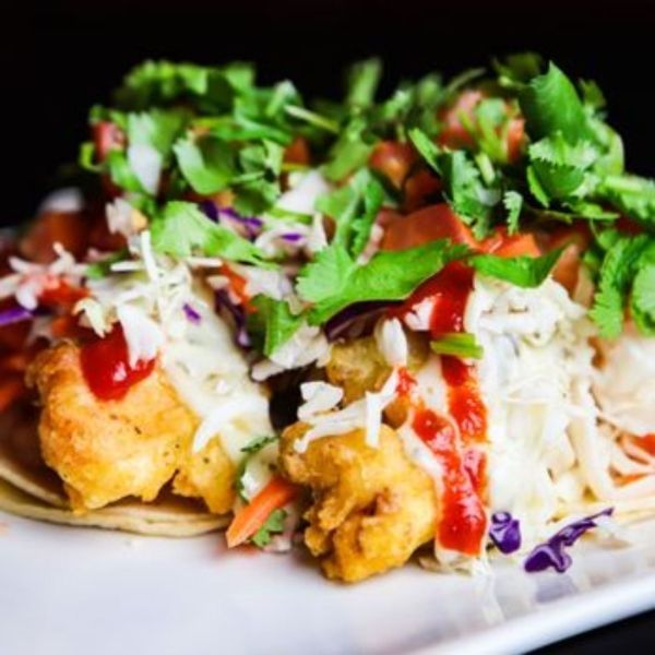 Close-up of a fish taco with fried fish, slaw, salsa, cilantro, and red sauce.