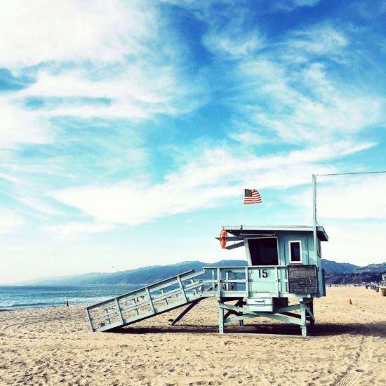 Lifeguard stand on a sandy beach under a blue sky with an American flag.