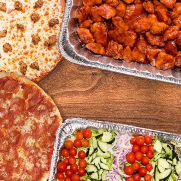 Pizza, chicken, and salad trays on a wooden table.