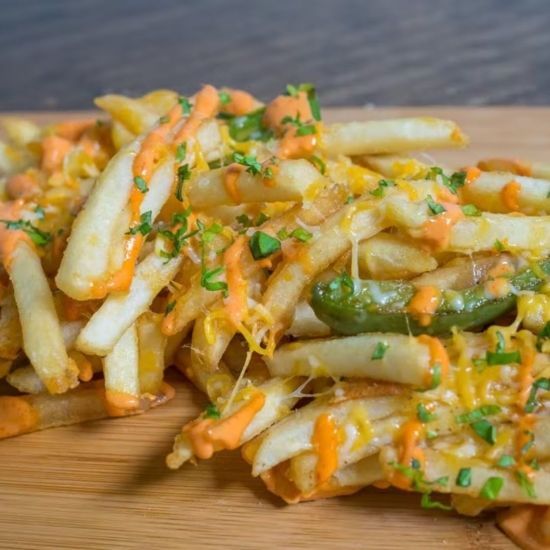 Fries topped with cheese, sauce, jalapeños, and herbs on a wooden board.