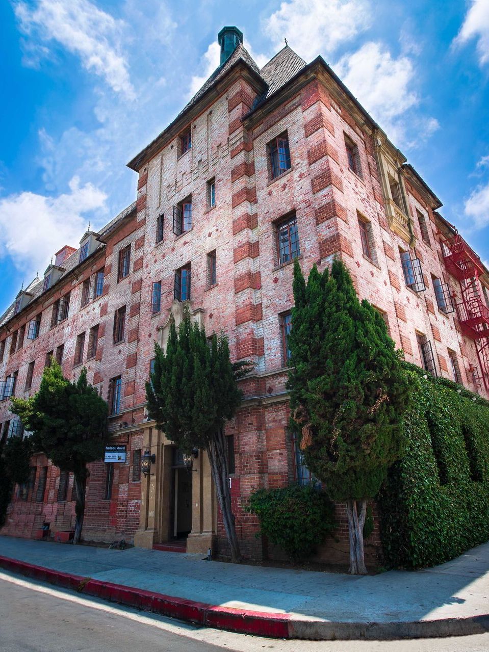 Red brick apartment building with green shrubbery against a blue sky.