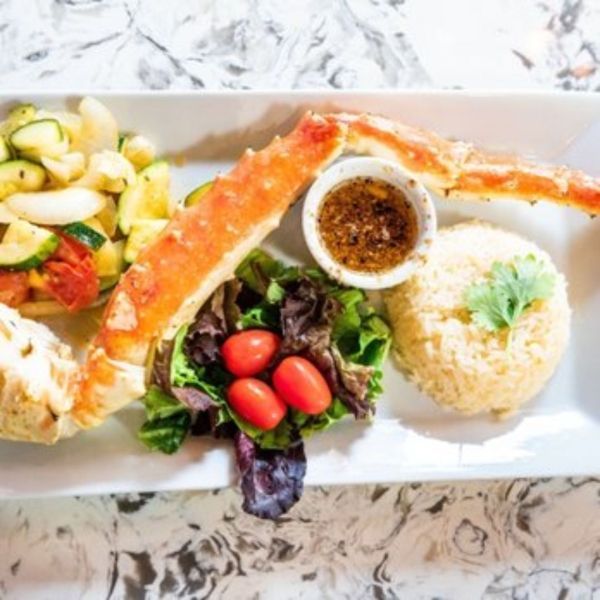 King crab leg with sides of vegetables, salad, rice, and dipping sauce.