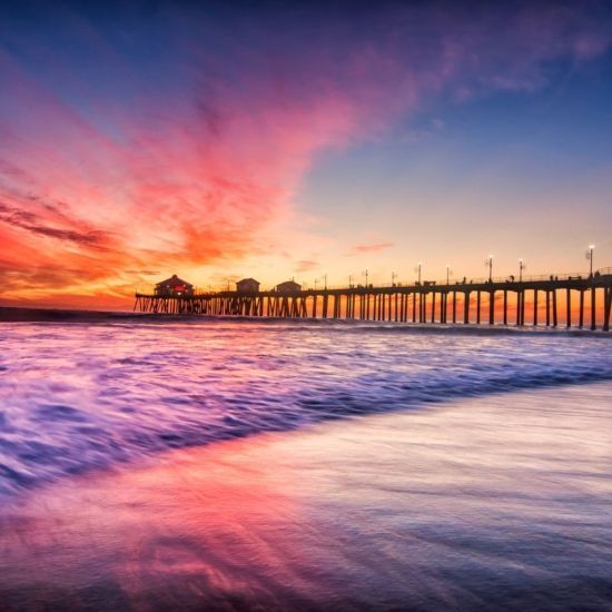 Sunset over ocean with pier silhouette; pink, orange, and purple sky reflecting on the water.