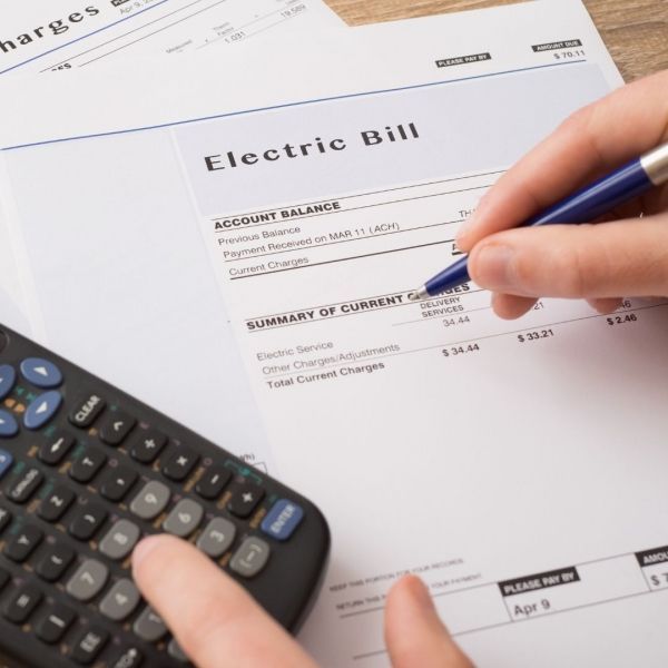 Person's hand with pen writing on an electric bill, calculator beside the bill.