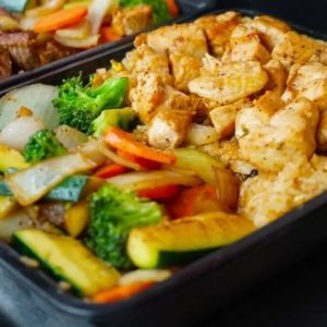 Chicken and vegetable stir-fry with rice in a black container.