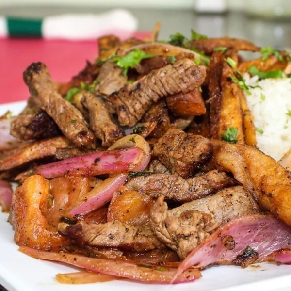 Peruvian Lomo Saltado: beef strips, onions, fries, and rice on a white plate, garnished with cilantro.