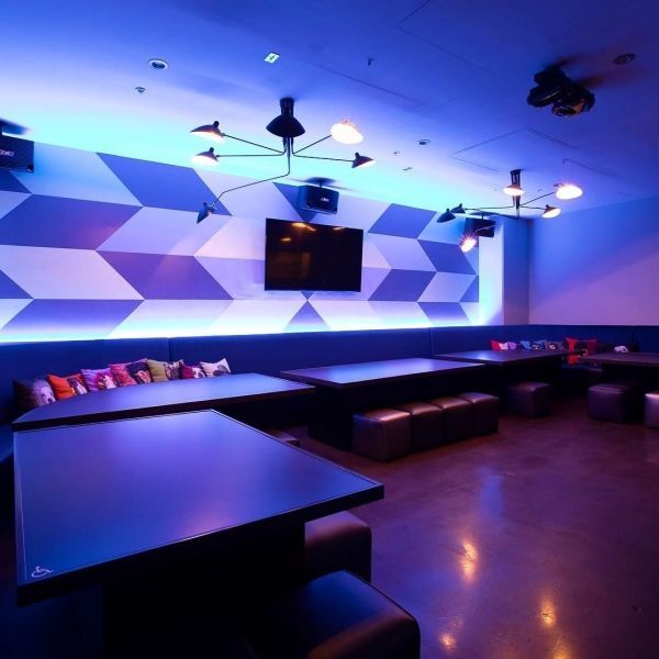 Karaoke room with geometric wall design, black tables, and blue lighting.