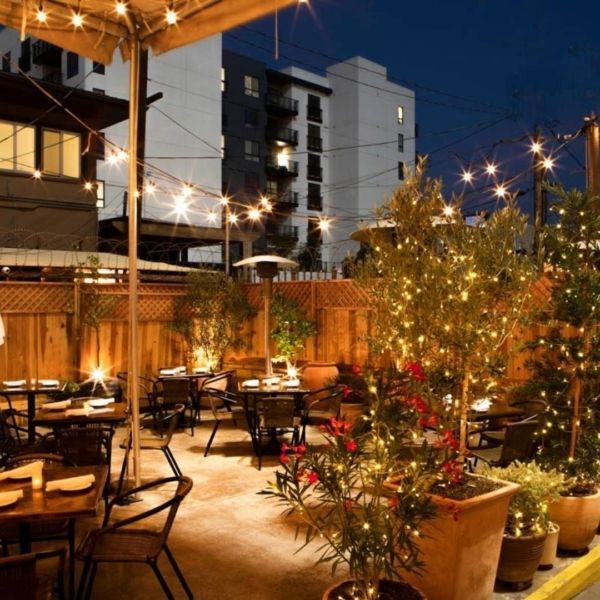 Outdoor restaurant patio at night with string lights, tables, and plants.