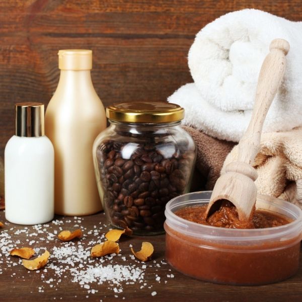 Spa products on a wooden table: lotions, towels, coffee beans, body scrub, and salt.