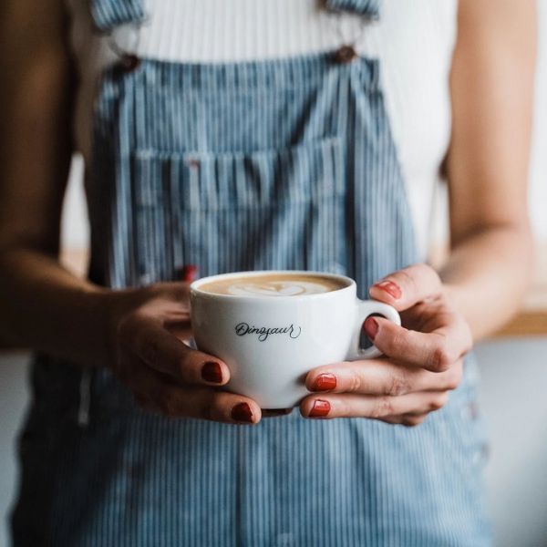 Woman in blue overalls holds a white coffee cup with 