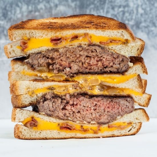 Stacked burger with cheese, bacon, and grilled onions on toasted bread.