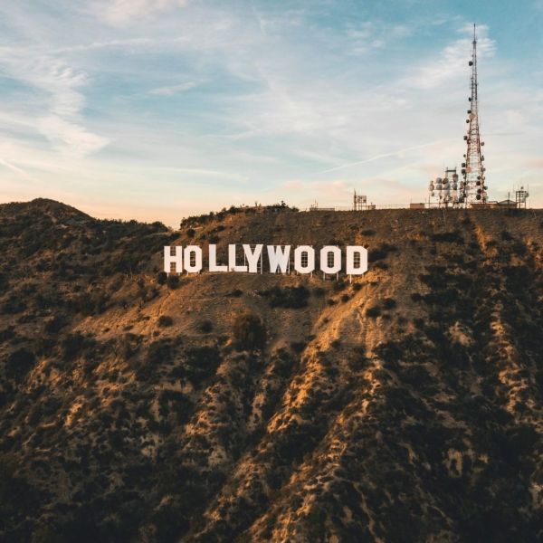 Hollywood sign on a hillside with a communication tower against a cloudy sky.