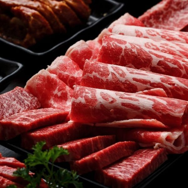 Sliced raw beef arranged on a black plate, showcasing marbling.
