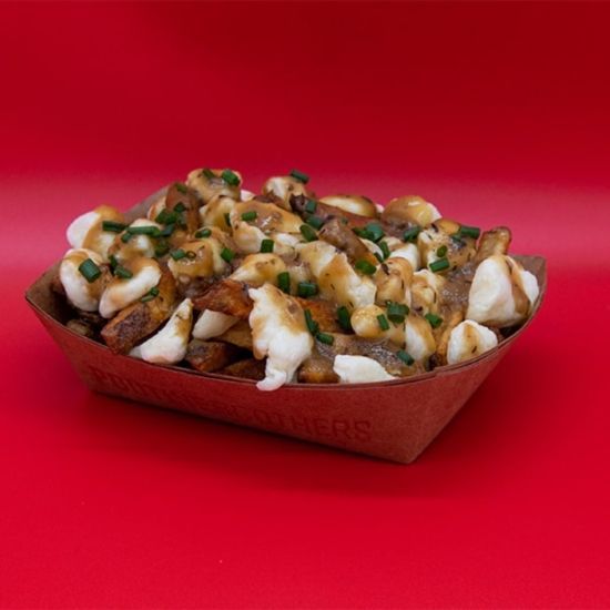 Poutine in a brown paper container, red background. French fries, cheese curds, gravy, and green onions.