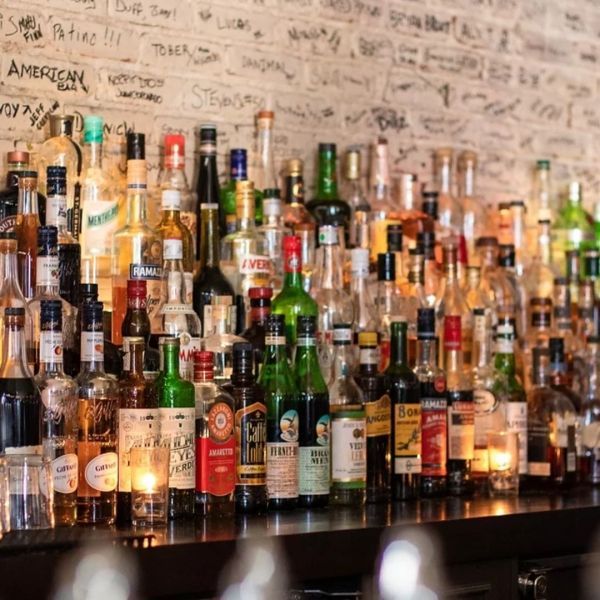 Bar with many liquor bottles on display, dimly lit. A wall above the bottles has graffiti.