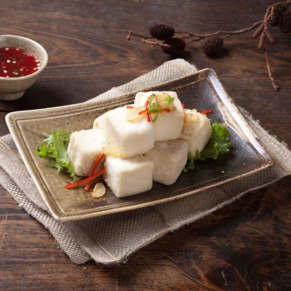 Fried tofu cubes on a plate with red chili sauce, garnished with scallions, set on a wooden surface.