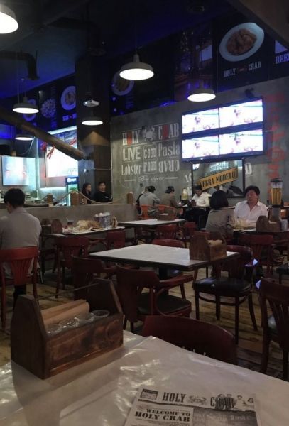 Interior of a restaurant with tables, chairs, and people dining. TVs and signs adorn the walls.