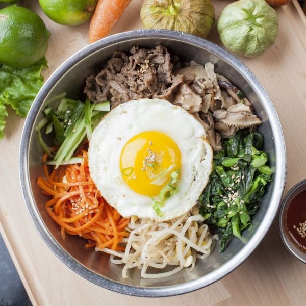 Bibimbap in metal bowl with egg, beef, vegetables, and sauce.