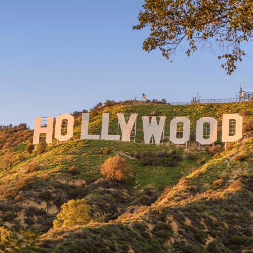 Hollywood sign on a sunny hillside. White letters on green, brown landscape, under a blue sky.