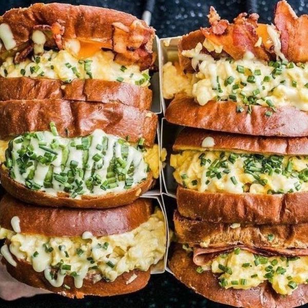 Two stacks of brioche egg sandwiches, with bacon and chives.