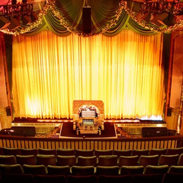 A theater stage with gold curtains, a pipe organ, and rows of seats.