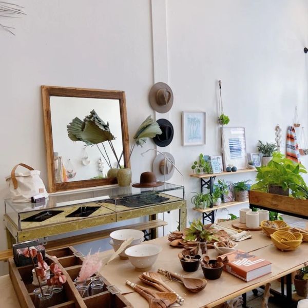 Interior of a shop with a display table of items like bowls and books, plants, and hats on the wall.