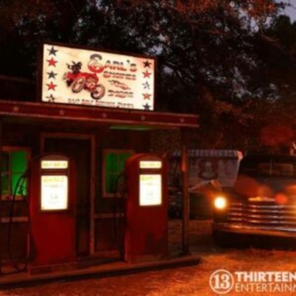 Gas station at dusk with illuminated pumps and vintage truck. Sign says 