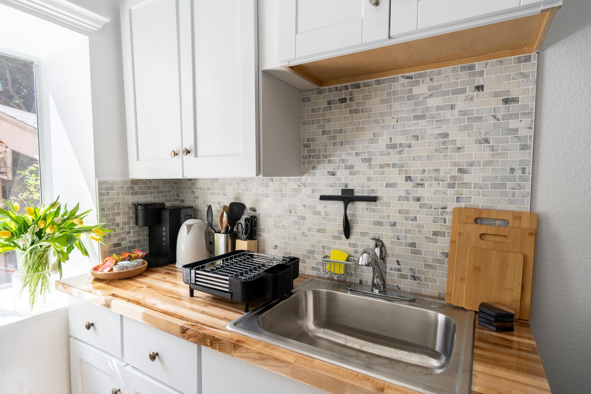 Small kitchen with white cabinets, wood countertops, a stainless steel sink, and mosaic backsplash.