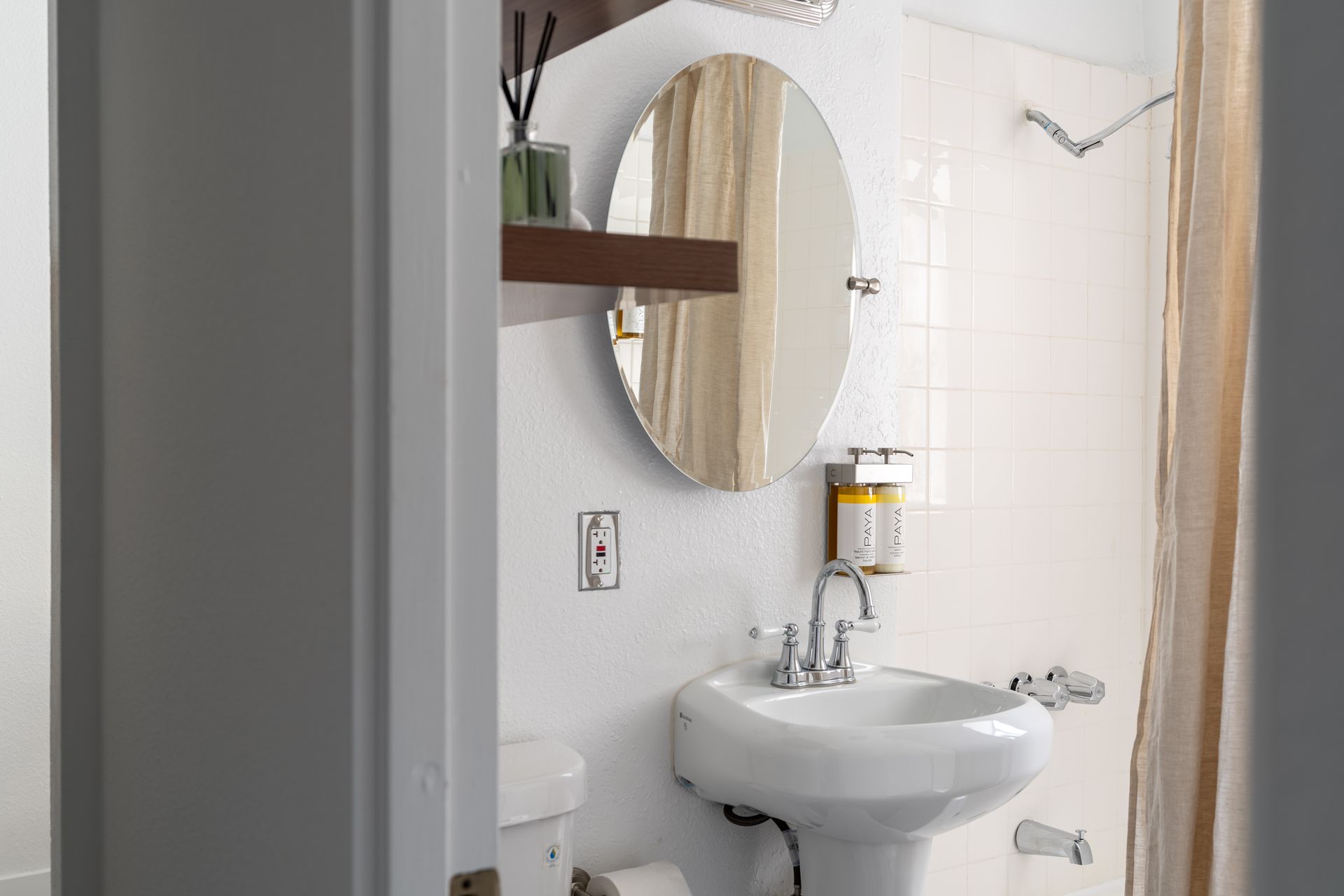Small, white bathroom with pedestal sink, oval mirror, and shower curtain.